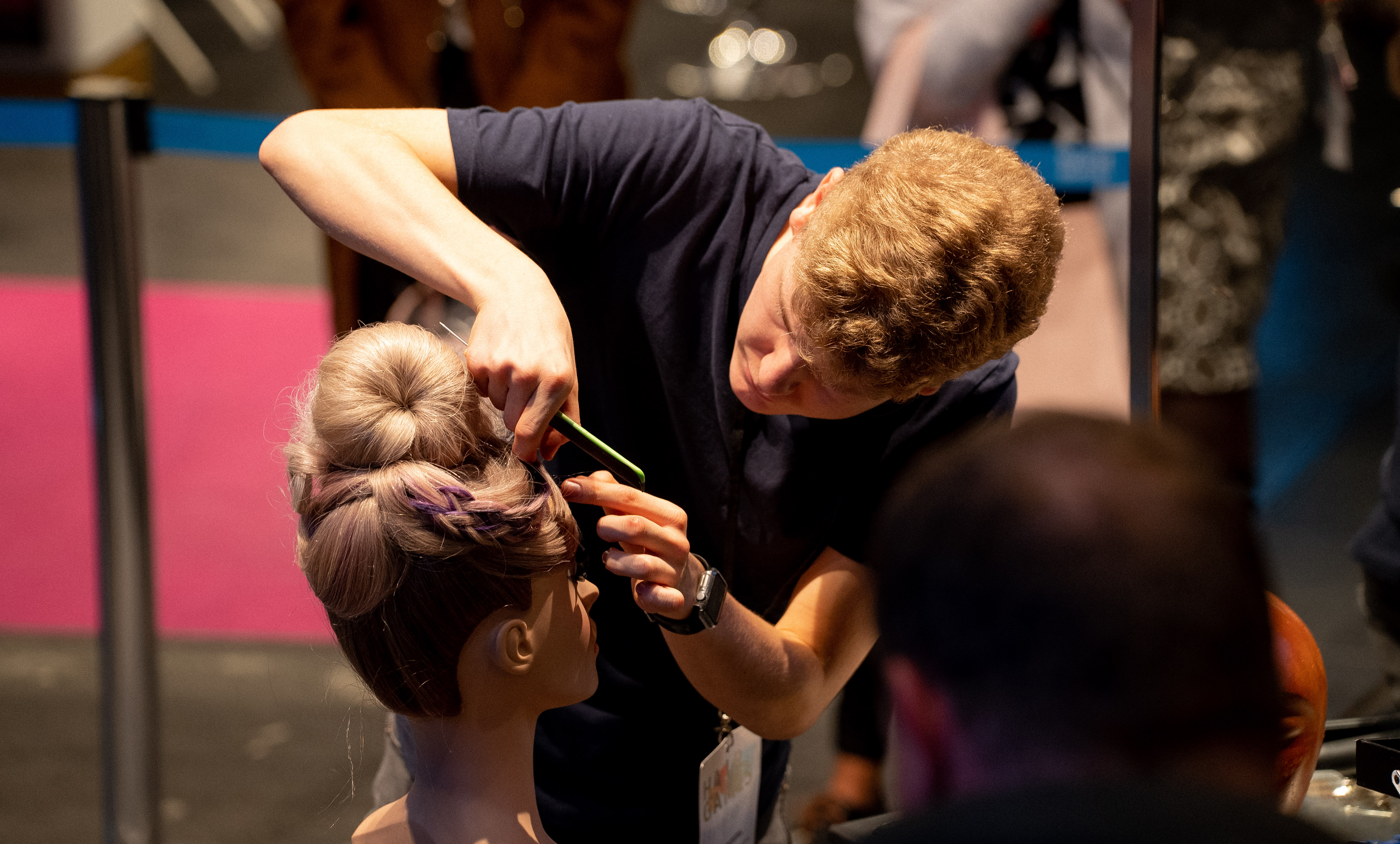 A hairdresser artfully puts hair of the forehead part on a training head, partly an updo can be seen