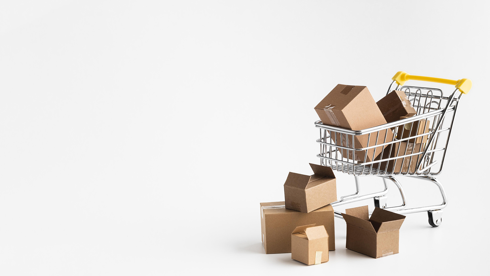 In the right half of the picture there is a shopping cart in front of a white background, filled with cardboard boxes, some cardboard boxes are lying on the floor in front of the cart